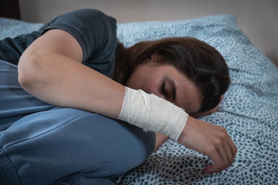 A young women with a bandaged wrist who looks distraught laying down.