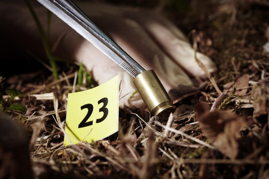 Photo of a crime scene technician picking up a bullet shell casing for evidence. 