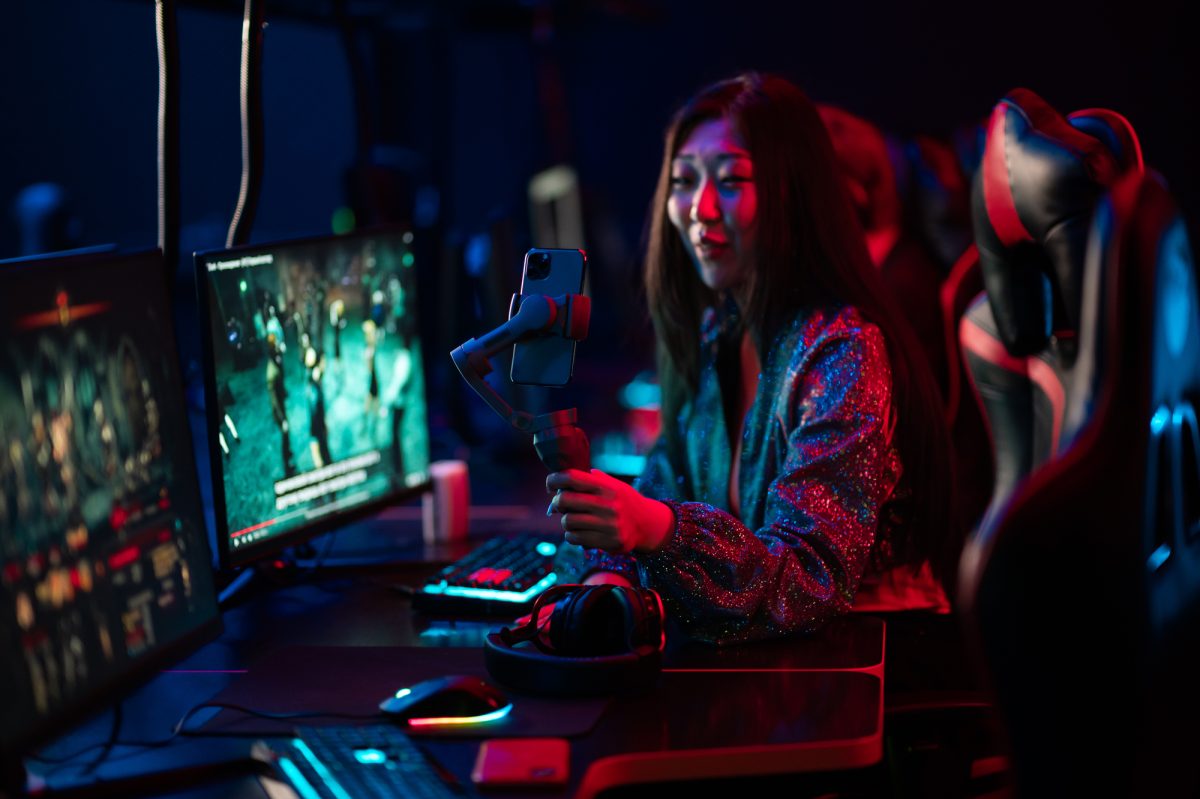 Neon light in the esports arena. Portrait of a young asian girl with a gimbal, who records a video blog content on a smartphone.