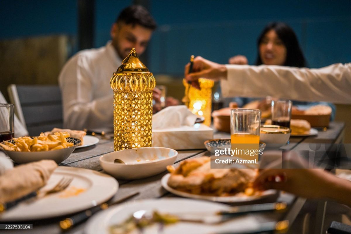 Young Arabic friends gather on a rooftop at night to share a Ramadan dinner. The table is adorned with a glowing lantern, diverse traditional dishes, and drinks, creating a warm and festive atmosphere under the dark sky. (Photo by Azman L / AFP) (Photo by AZMAN L/AFP via Getty Images)